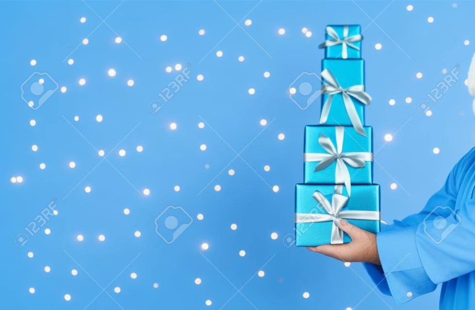 Santa tenendo i contenitori di regalo di Natale su uno sfondo azzurro brillante