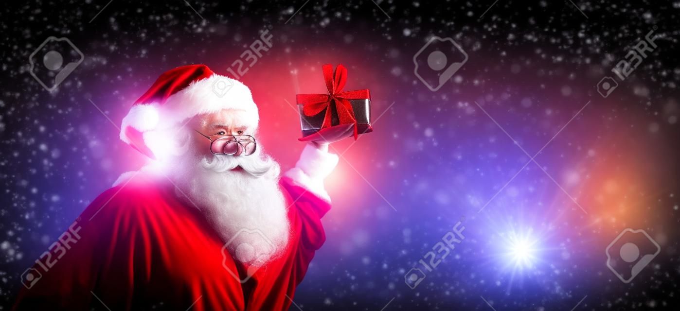 Santa holding a Christmas gift on a shiny light background