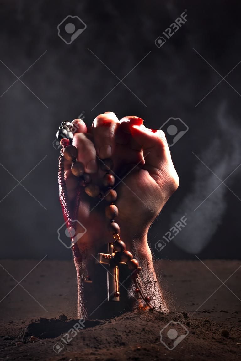 Human hand in blood and dirt with rosary on dark background