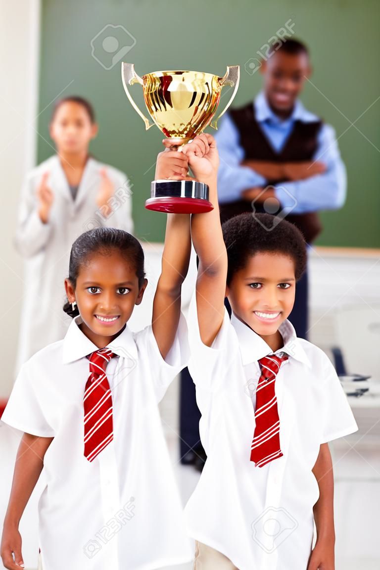 two elementary students holding a trophy in classroom