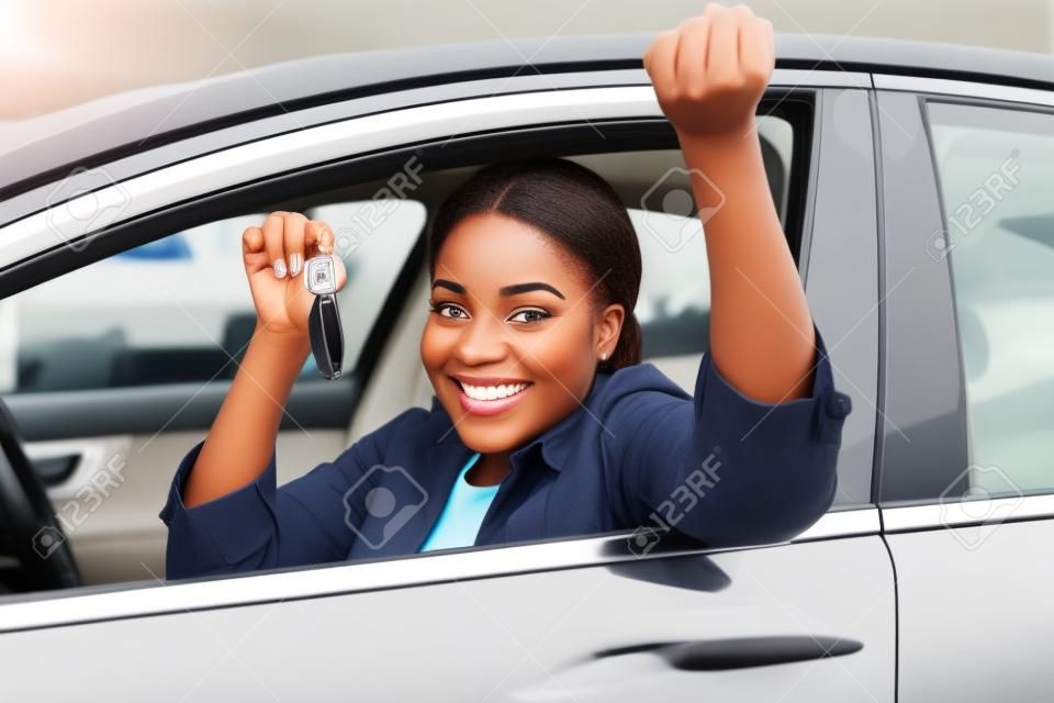 vrolijke jonge Afrikaanse vrouw toont haar nieuwe autosleutel bij dealership