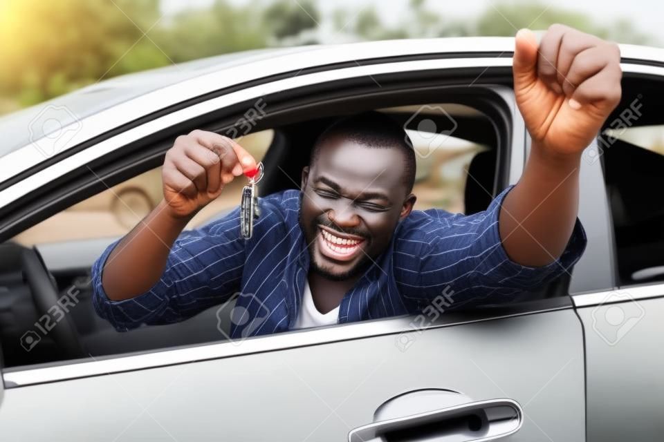 Hombre africano emocionado mostrando una llave del coche dentro de su vehículo nuevo
