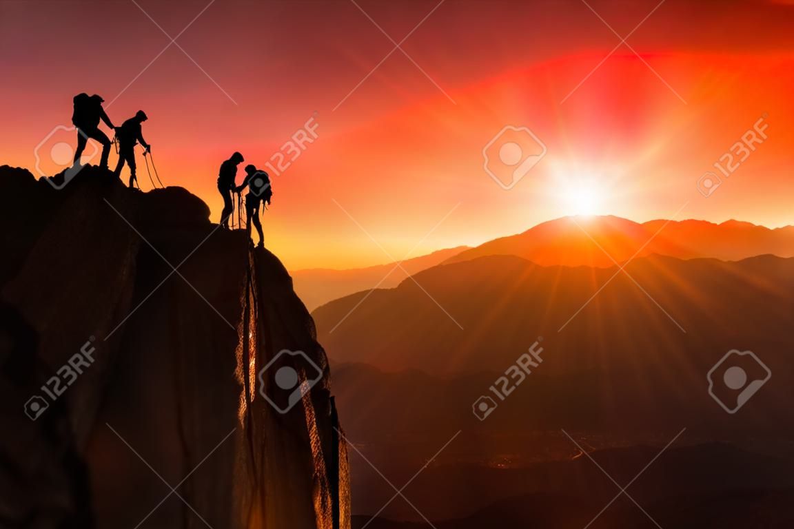 Team der Bergsteiger helfen, den Gipfel in Teamarbeit in einer traumhaften Berglandschaft bei Sonnenuntergang zu erobern