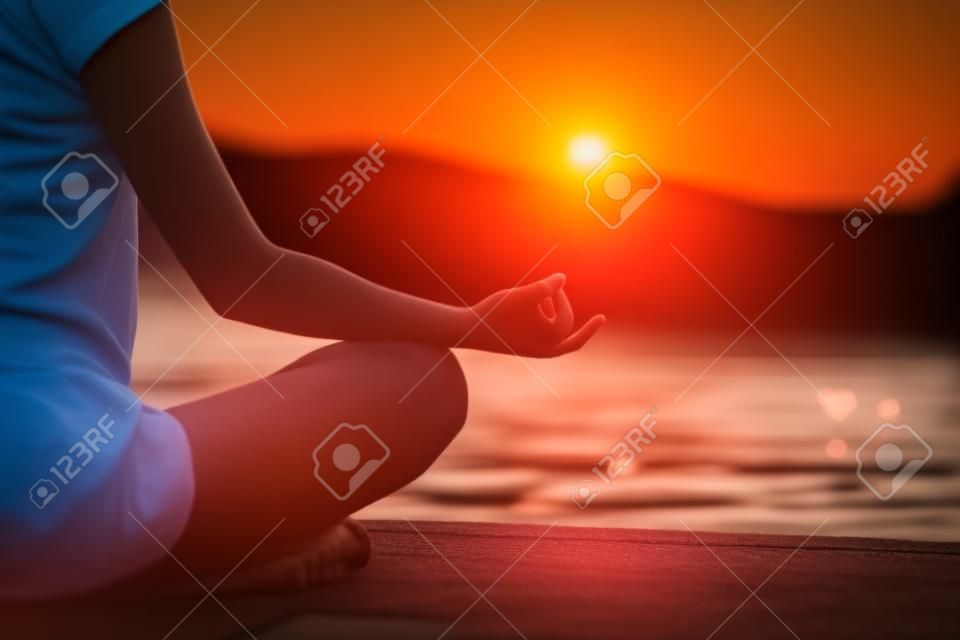 Meditando junto al lago, sentado en posición de loto, la puesta del sol, relajado, atención selectiva, cómodo espacio de la copia