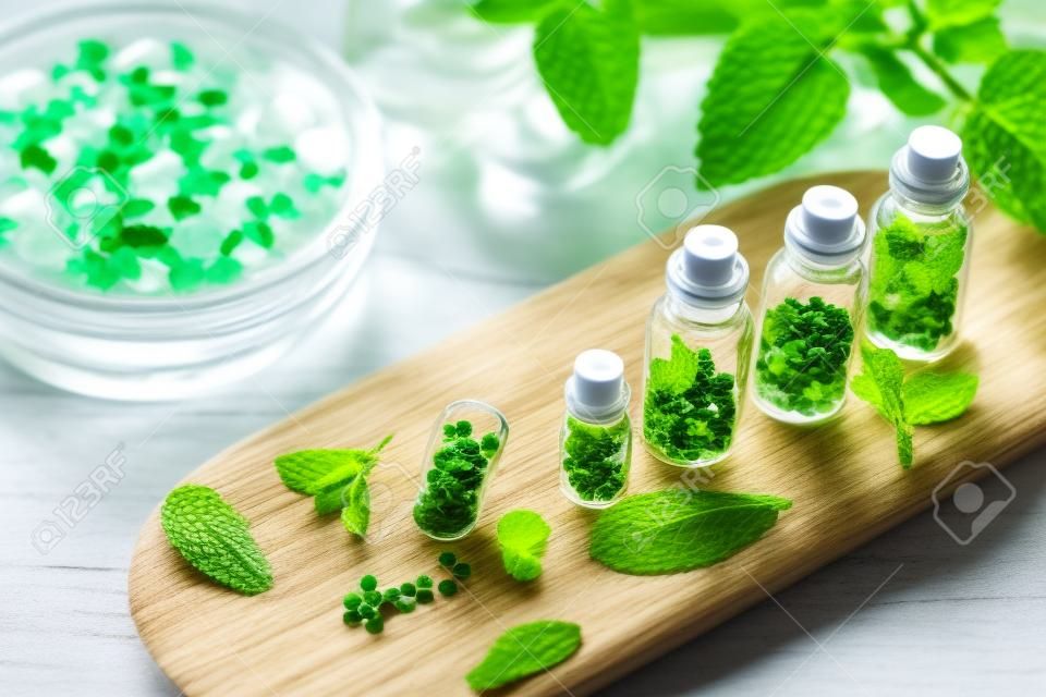 Homeopathic globules in small bottles with mint leaves in background, homeopathy concept