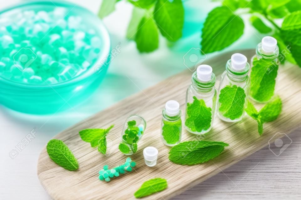 Homeopathic globules in small bottles with mint leaves in background, homeopathy concept