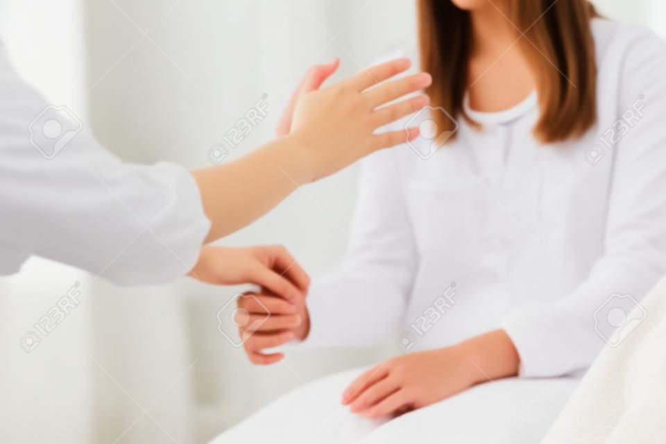 젊은 여성 환자와 대체 요법 치료를 수행하는 여성 치료 치료사. 손을 잡고 적용 및 근육 테스트를 하는 치료사. 흰 옷을 입고.