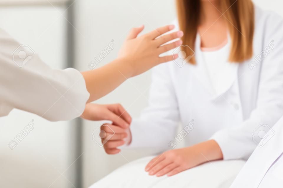 젊은 여성 환자와 대체 요법 치료를 수행하는 여성 치료 치료사. 손을 잡고 적용 및 근육 테스트를 하는 치료사. 흰 옷을 입고.
