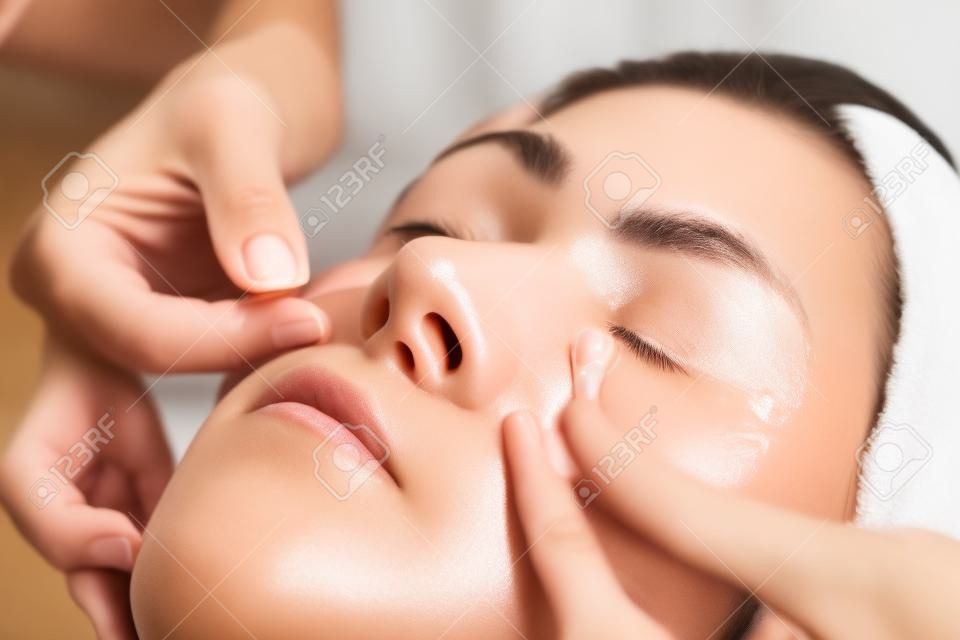 Masaje facial para ojeras. Primer plano de una mujer joven que recibe un masaje facial de drenaje linfático con palos