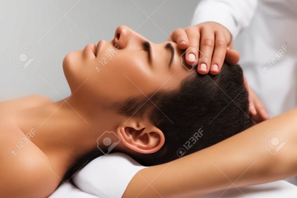 頭蓋仙骨療法マッサージ。女性の額をマッサージするセラピスト。