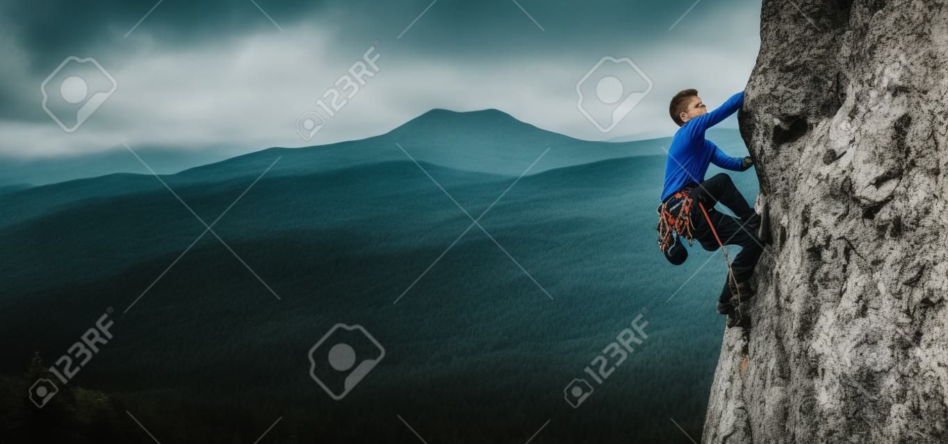 Jongeman klimt op een rotsachtige muur in een vallei met bergen