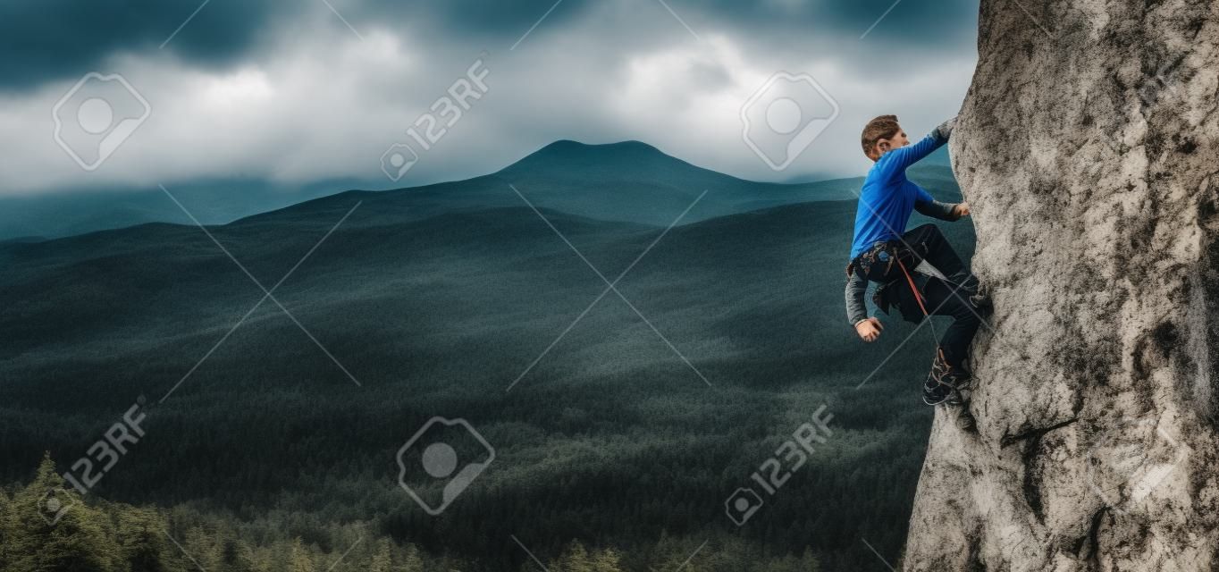Jongeman klimt op een rotsachtige muur in een vallei met bergen
