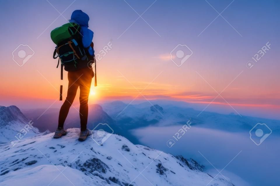 Randonneur avec sac à dos détente sur le dessus d'une montagne et en savourant le panorama de la vallée au lever du soleil