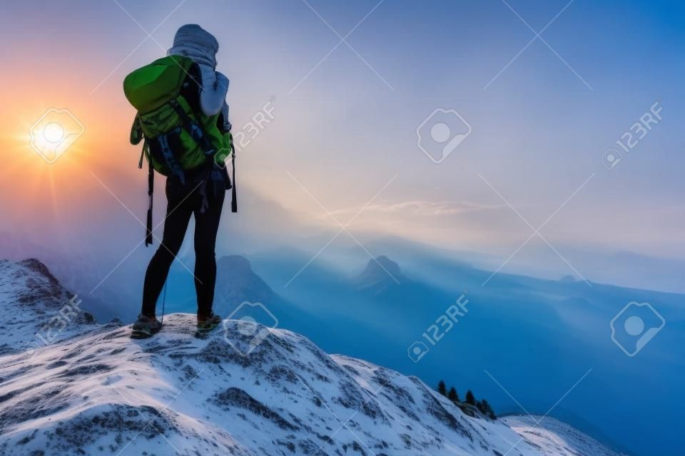 Turysta z plecakiem, relaks na szczycie góry i cieszyć widokiem na dolinę podczas wschodu słońca
