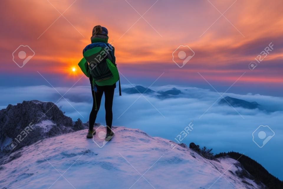 Lady Wanderer mit Rucksack steht auf dem Gipfel eines Berges und genießen Sonnenaufgang
