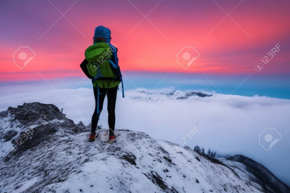 Señora caminante con mochila de pie en la cima de una montaña y disfrutar de la salida del sol
