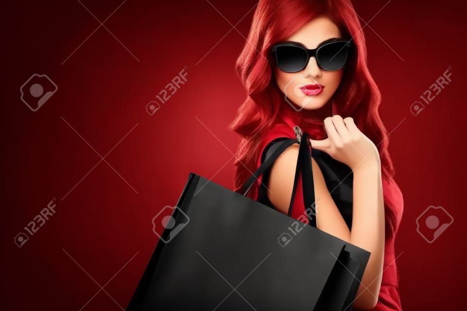 美しい若い女性は、黒い金曜日の休日のショッピングを確認します。暗い背景に黒いバッグを持つ少女。