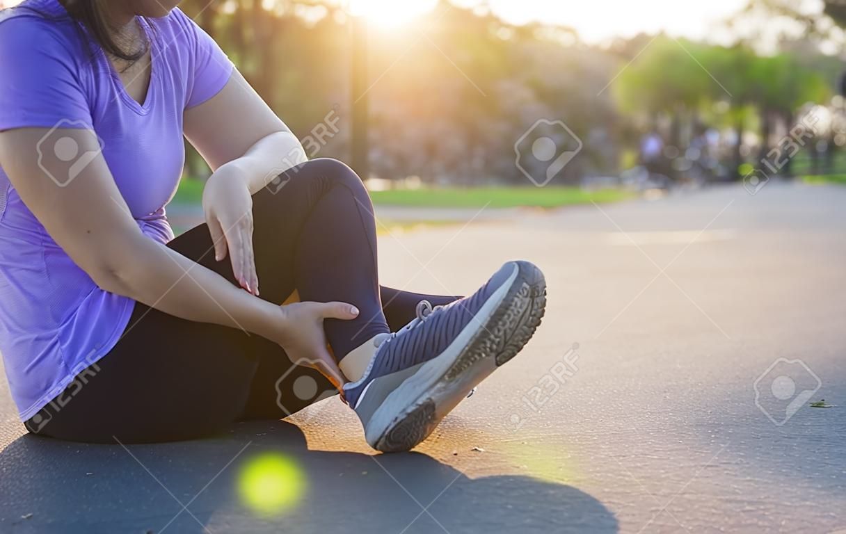 Young woman massaging her painful legs from jogging and running in the park. Sport and exercise concept.