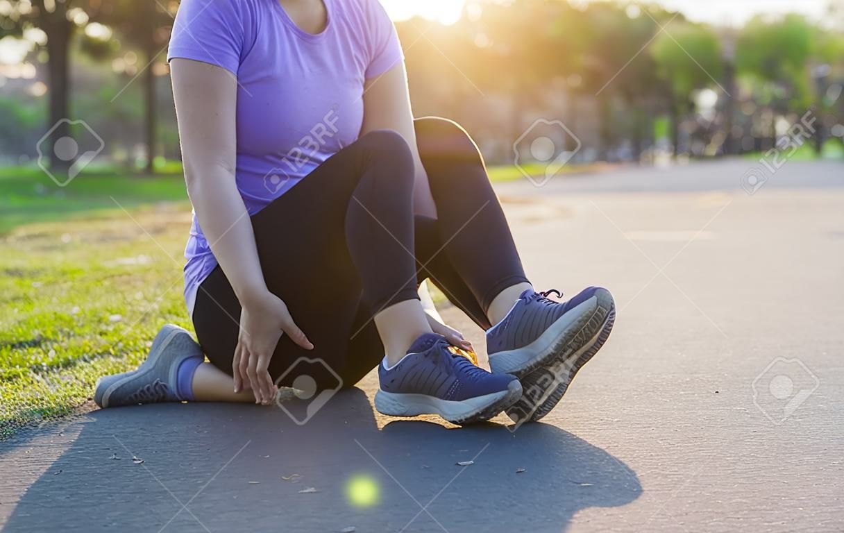 Mujer joven masajeando sus piernas dolorosas de trotar y correr en el parque. Concepto de deporte y ejercicio.