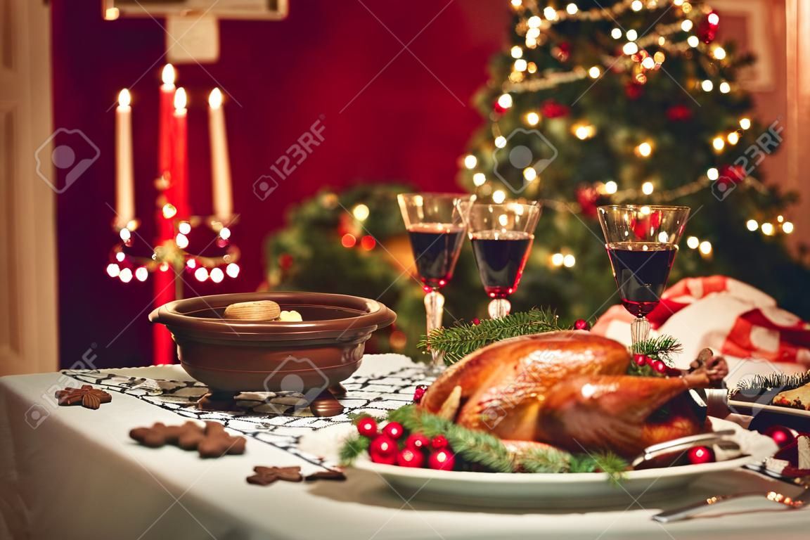 dîner de Noël aux chandelles, décor de table. table de Thanksgiving avec la dinde cuite au four dans une salle décorée avec un arbre de Noël.