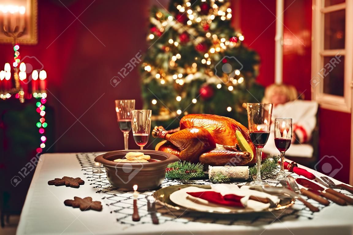 dîner de Noël aux chandelles, décor de table. table de Thanksgiving avec la dinde cuite au four dans une salle décorée avec un arbre de Noël.