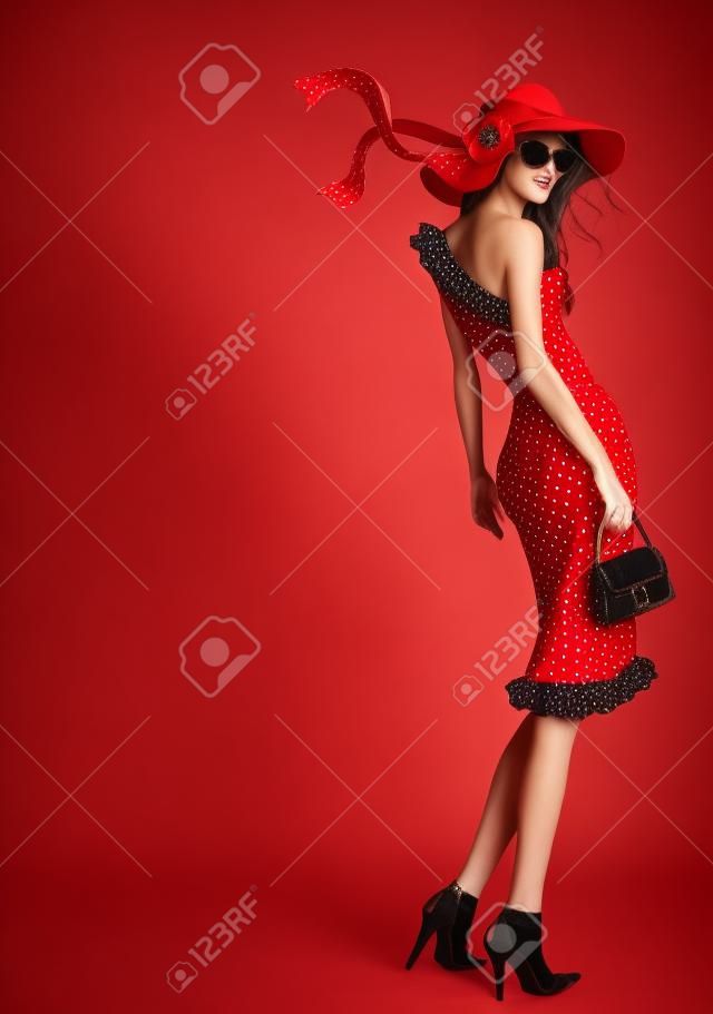 Kırmızı şapka ve puantiyeler elbise giymiş güzel bir genç kadın ayakta