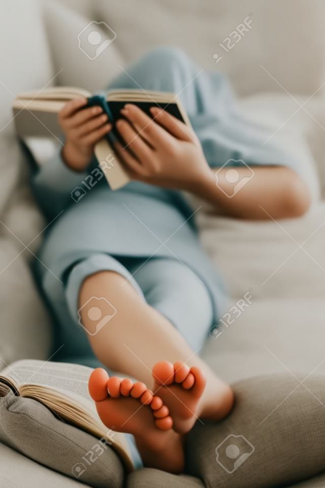 Barefoot jeune femme allongée sur le canapé et la lecture du livre