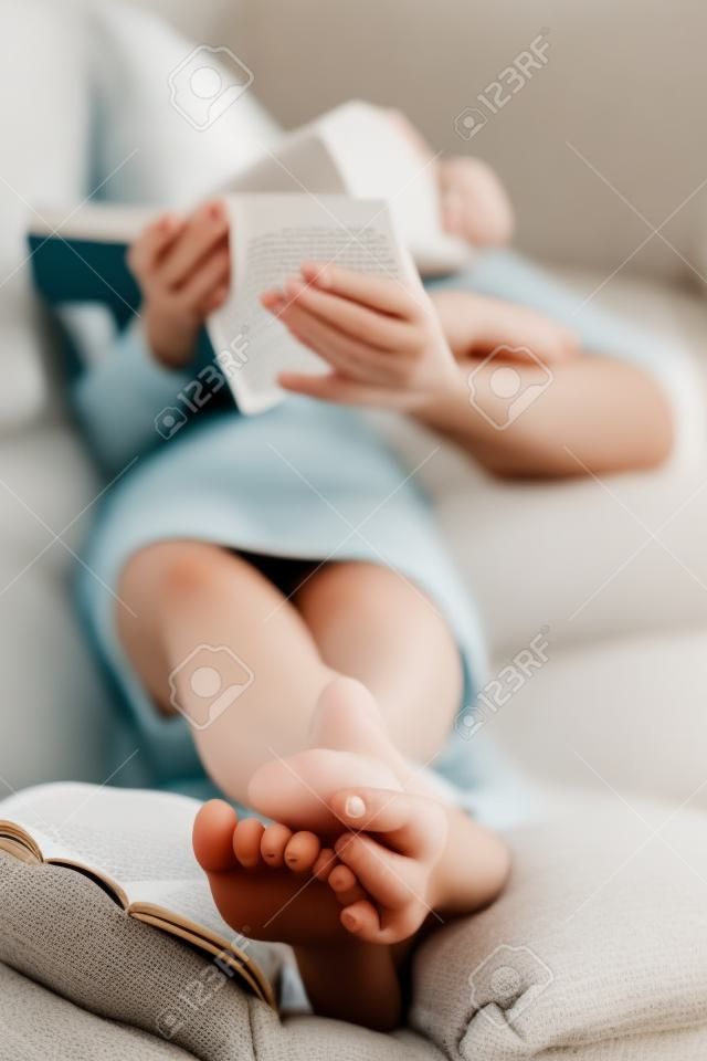 Barefoot junge Frau auf Sofa liegend und Lesebuch