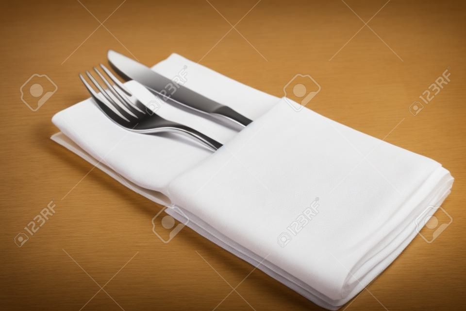 Fork and knife lie on a folded white napkin in the restaurant.