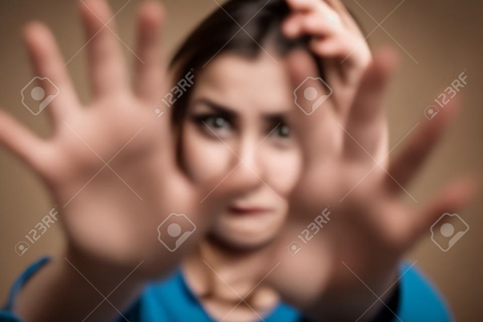 Young abused woman defending with pray looking at camera with outstretched arm. Selective focus. Focus on background, on woman face.