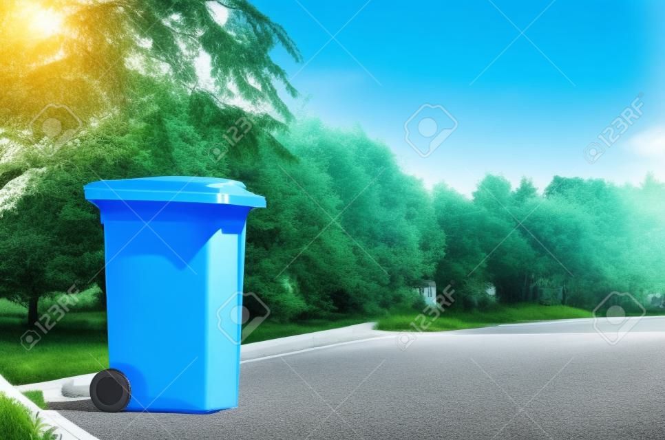 Unloocked big empty blue plastic trash garbage bin in front of the modern house with green trees. No public trash on the side of the road. Infectious control, garbage disposal of waste concept