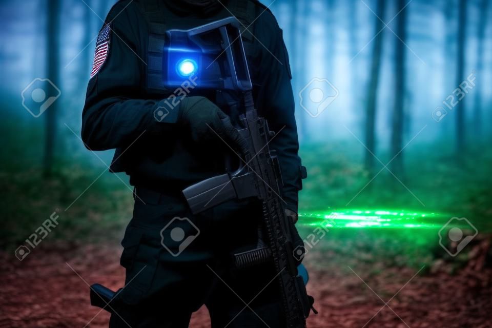 Midsection of unknown man standing in the woods in nature wearing black special forces military or police uniform playing laserwar lasertag airsoft game holding rifle replica infrared sensor laser tag