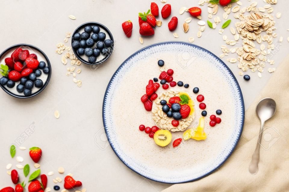 Healthy breakfast, dieting and detox concept - wholegrain fresh oatmeal porridge on plate with fruits, berries and nuts on beige background. Still life, top view