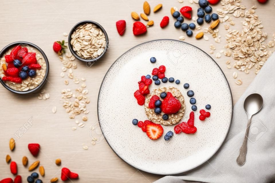 Healthy breakfast, dieting and detox concept - wholegrain fresh oatmeal porridge on plate with fruits, berries and nuts on beige background. Still life, top view