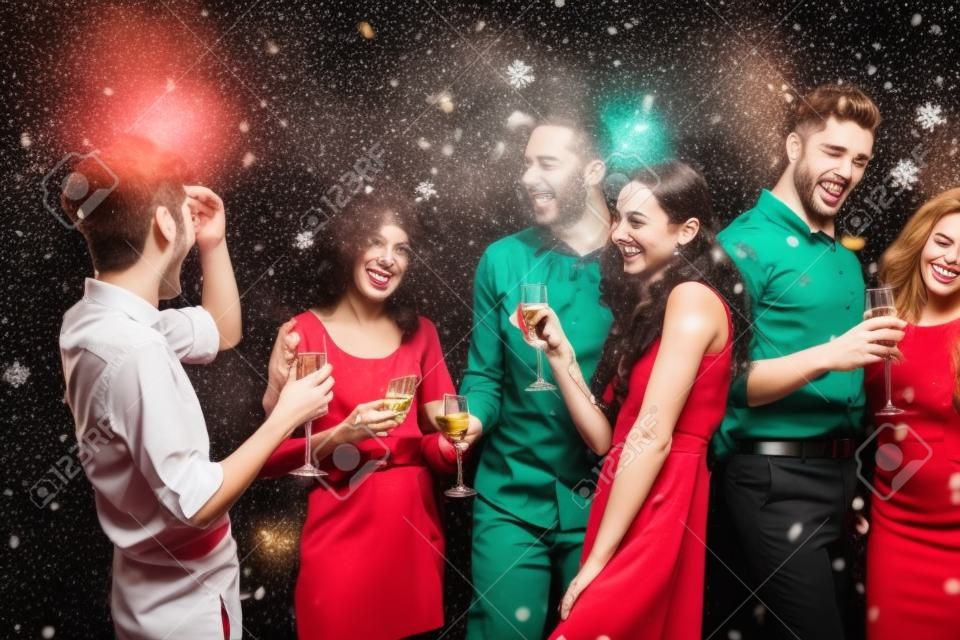 Wigilia w biurze. grupa radosnych kolegów bawiących się podczas obchodów nowego roku. szczęśliwi uśmiechnięci młodzi ludzie pijący szampana i cieszący się życiem.