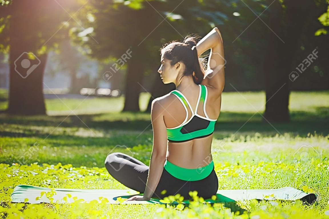 Fitness, Frauentraining Yoga in Kuhkopfhaltung im Freien. Junges schlankes Mädchen macht Übung. Wellness, Ruhe, Entspannung, gesundes, aktives Lifestyle-Konzept, Rückansicht