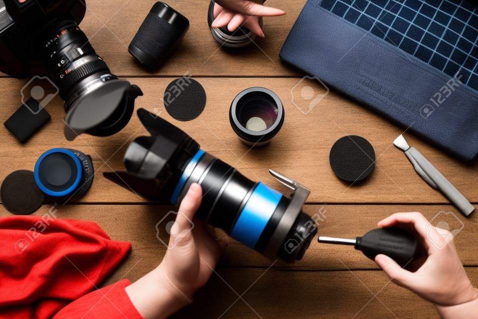 Camera lens cleaning with special tool, close-up. Photographer hands sweeping lens on workplace . Professional photographing equipment care, technology concept