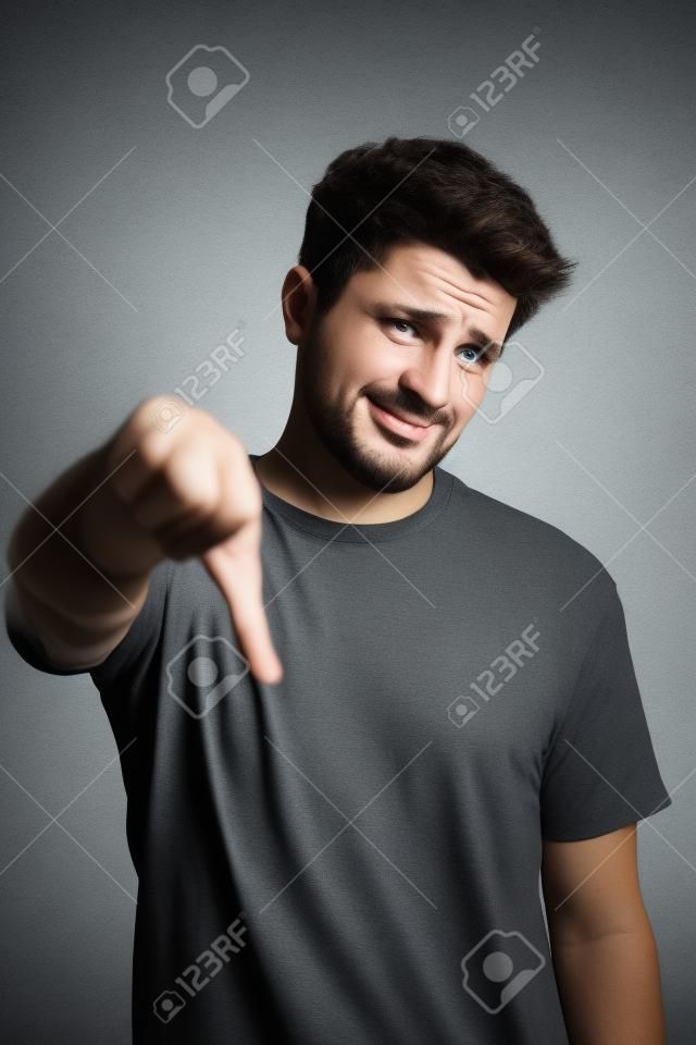 Unhappy man showing thumb down sign. Dissapointment, rejection concept, studio shot at gray background, copy space