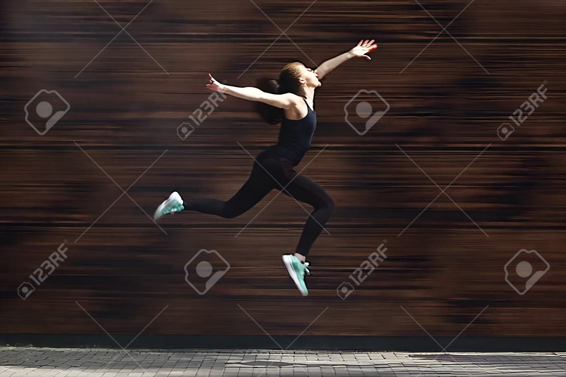 Belle jeune femme sautant contre un mur en bois sombre, s'amusant, copiez l'espace. Concept d'esprit de liberté