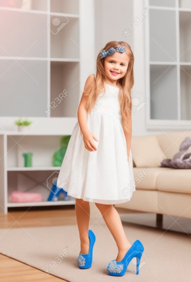 Bambina graziosa con le scarpe di mamme. Piccolo fashionista cercando su tacchi alti a casa, copia dello spazio
