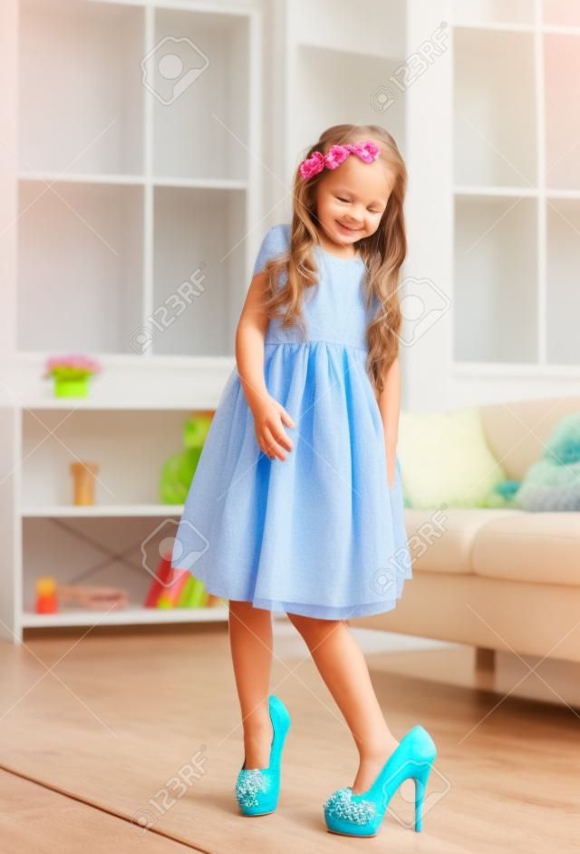 Bambina graziosa con le scarpe di mamme. Piccolo fashionista cercando su tacchi alti a casa, copia dello spazio