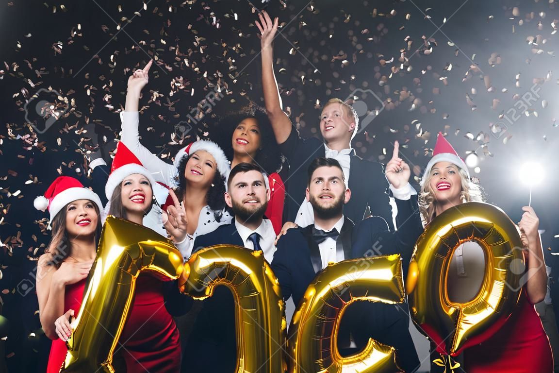 Office christmas party. Group of joyful colleagues having fun at new year celebration, holding golden number balloons, 2019 year symbol, looking upwards