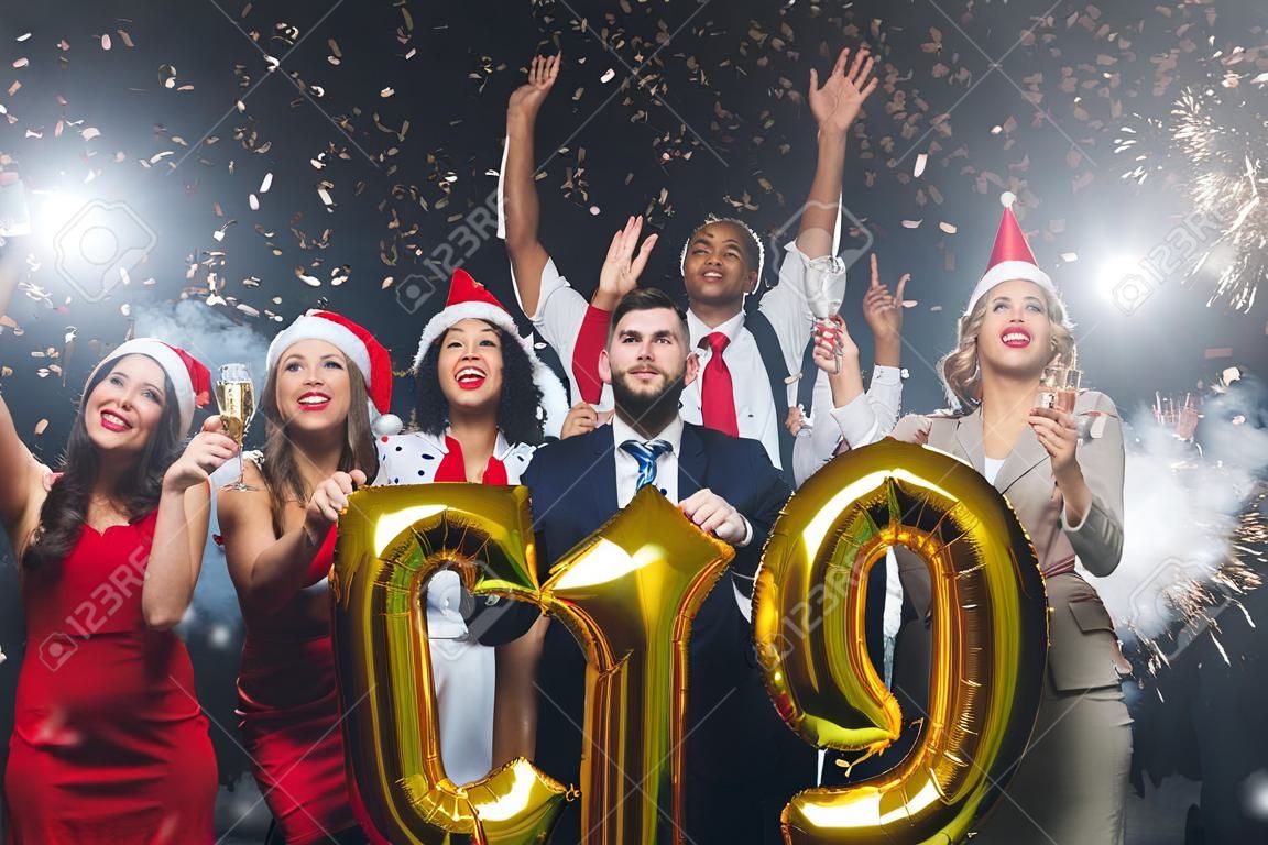 Festa di Natale in ufficio. Gruppo di colleghi gioiosi che si divertono alla celebrazione del nuovo anno, con in mano palloncini con numero d'oro, simbolo dell'anno 2019, guardando verso l'alto