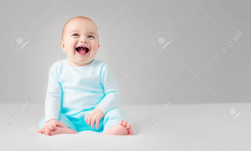 Delightful neonate laughing, sitting on bed on white background, copy space