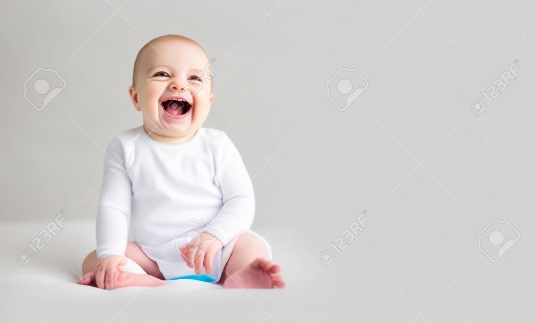 Delightful neonate laughing, sitting on bed on white background, copy space