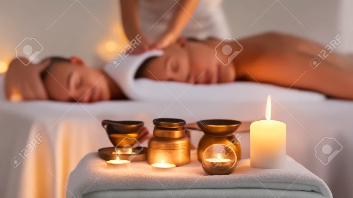 Relaxed woman enjoying aromatherapy massage in luxury spa with candle on foreground