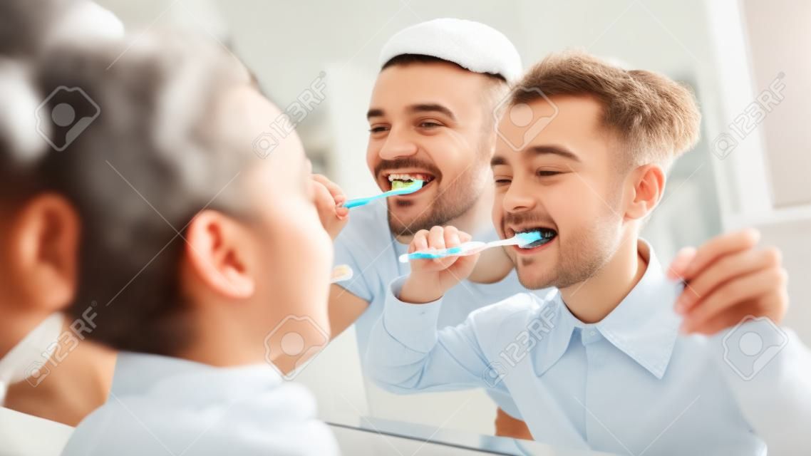Little Daughter And Father Brushing Teeth Together In The Morning, Looking At Mirror