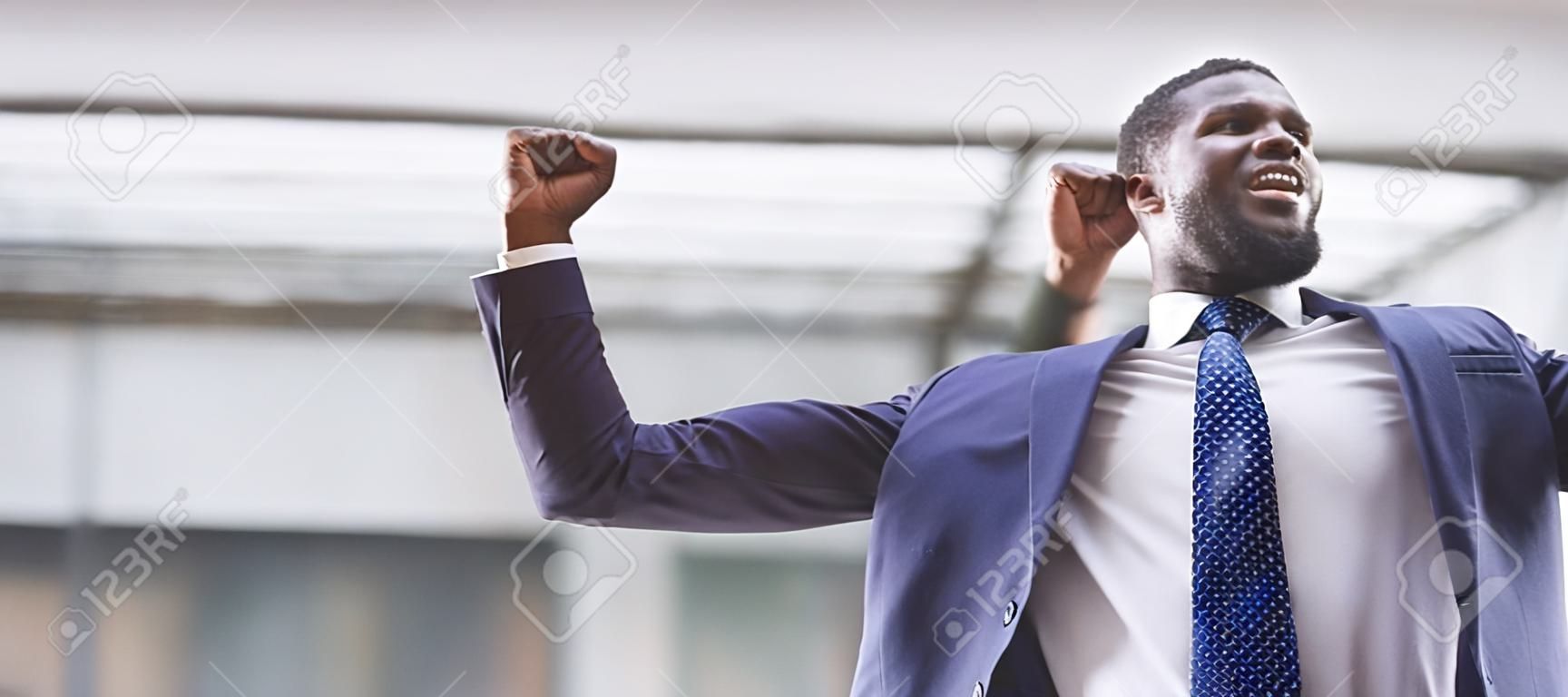 Przystojny Afroamerykanin potrząsający zaciśniętymi pięściami świętujący panoramę sukcesu biznesowego z wolną przestrzenią