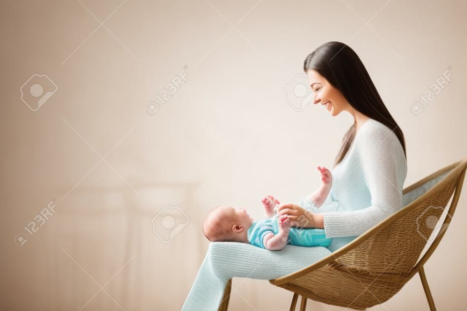 Adorável bebê bebê deitado no colo de sua mãe que sentado na cadeira de vime em casa, vista lateral com espaço livre