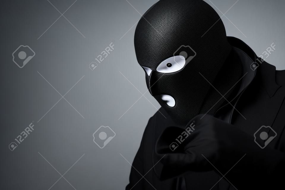 Closeup portrait of greedy disguised villain in black mask looking at something to steal, copyspace, white studio wall